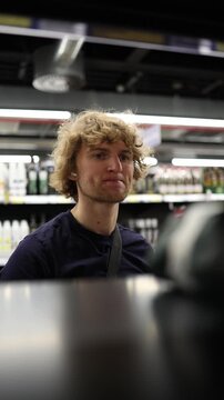 Vertical screen shopper reaches for a product on supermarket shelf but changes his mind and leaves it behind showing hesitation and reconsideration while grocery shopping
