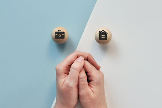 Conceptual top view of hands positioned between business and home symbols, representing the choice between office work and working from home
