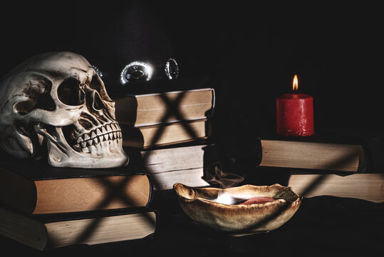 Human skull with wizard hat, old books and smoking potion by candlelight