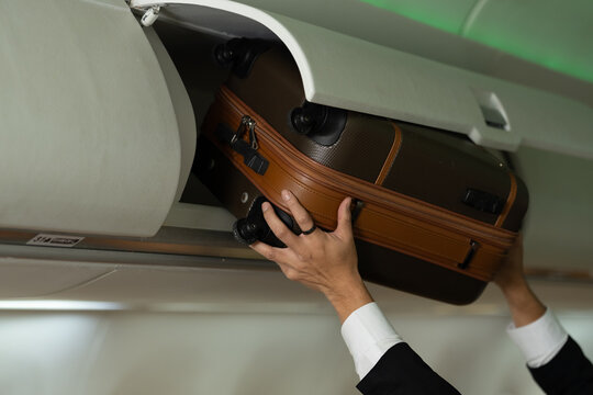 Passenger stowing suitcase inside overhead compartment of modern commercial aircraft cabin, representing baggage storage, boarding convenience, travel preparation, airline passenger experience.
