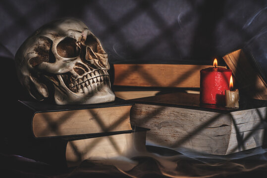 Human skull resting on old books with candles and mysterious smoke