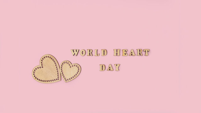 World Heart Day message with handcrafted wooden hearts and lettering on a soft pink background, expressing love and compassion through a warm minimalist design for greeting cards and social media
