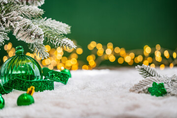 Naklejka premium A Christmas background featuring emerald baubles with gold filigree beneath a frosted pine branch, wrapped in glittering green ribbon on snow, set against deep green with twinkling lights.
