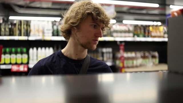 Shopper chooses a product from supermarket shelf carefully comparing available options and deciding what to buy during a routine grocery shopping visit for everyday needs