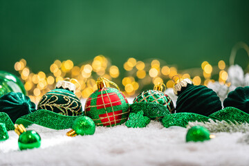Naklejka premium A Christmas background featuring green velvet baubles, a red and green plaid ornament, and a snowflake wrapped in glittering ribbon on snow, set against deep green with twinkling lights.
