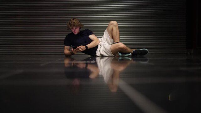 Young man lies with only a phone and personal style symbolizing modern youth owning almost nothing while digital identity replaces possessions in an empty space nowadays
