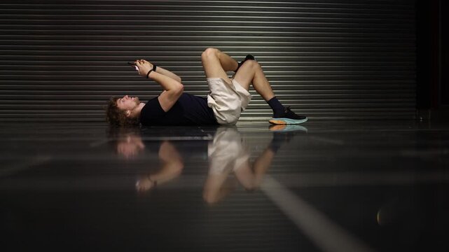 Student lies on the floor absorbed in his smartphone escaping into a digital world while ignoring his surroundings showing isolation screen dependence and modern solitude