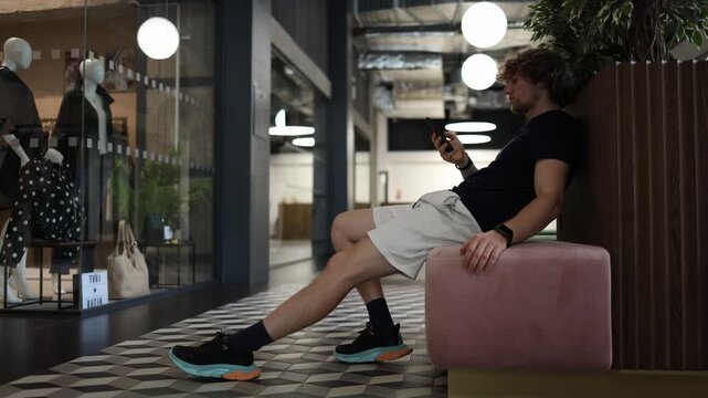 Lazy man sits idle scrolling on his phone avoiding action and responsibility while wasting time in inactivity and procrastination during an unproductive day indoors alone