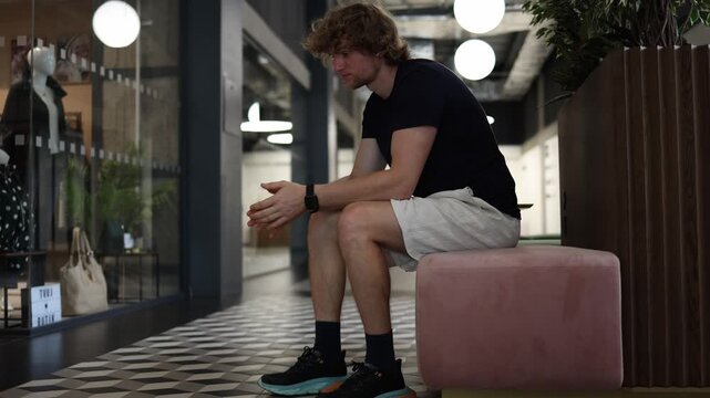 Stressed overworked man sits exhausted with head down struggling with burnout pressure and mental fatigue after long workday while resting alone in a modern shopping mall