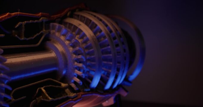 Slow tracking shot of turbine rotor blades rotating inside cutaway jet engine in studio with moody blue and warm rim lighting, macro probe view.