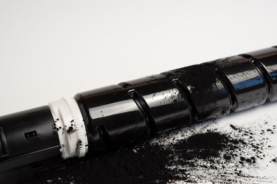 Black toner cartridge with spilled toner powder on white background, printer maintenance concept