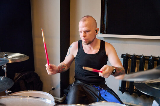 Adult male drummer rehearses behind drum kit under warm stage lighting