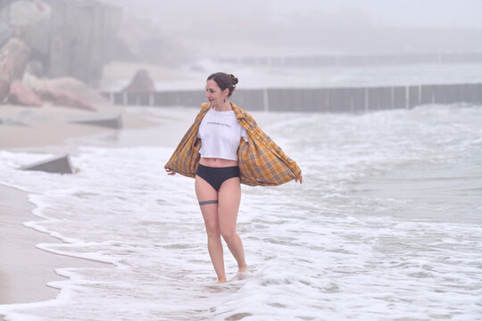 Young woman walking through misty sea surf along foggy beach