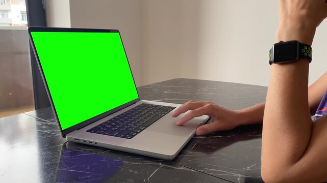 Person using laptop, side view, with chroma key display at a table, suitable for remote work, online services, software demonstrations, advertising, website mockups and digital interface replacement
