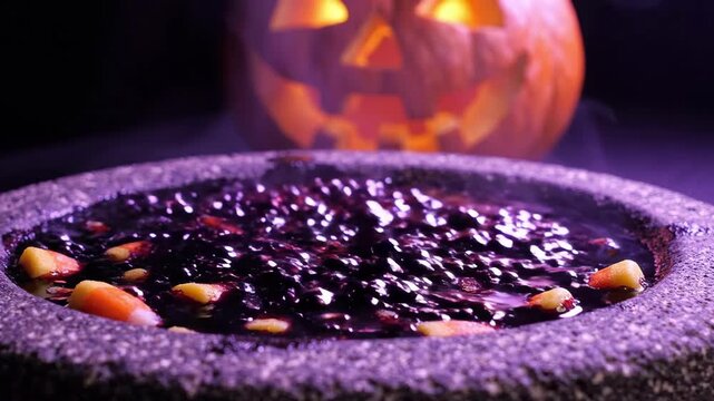 Spooky Halloween cauldron filled with dark swirling liquid and festive candy corn with a glowing jack o lantern in the eerie purple hazy background