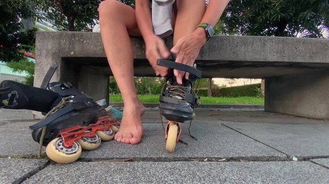 Woman fastening inline skates low angle beside a park bench, preparing for roller skating outdoors with secure boot adjustment for recreation, fitness training, urban mobility and active transport