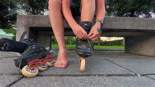 Person lacing inline skate, low-angle close-up beside a bench outdoors, showing preparation for rollerblading, recreational fitness, sports equipment use and active leisure before a skating session