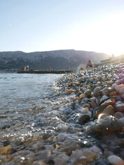 close up of some colorfoul pebbles being hit by the waves at a beach with people and mountains in the background in Baska, Croatia © Isabella