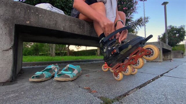 Skater fastening inline skate strap, low-angle close-up beside a park bench, showing secure footwear adjustment before skating for sports safety, equipment fitting, recreational training