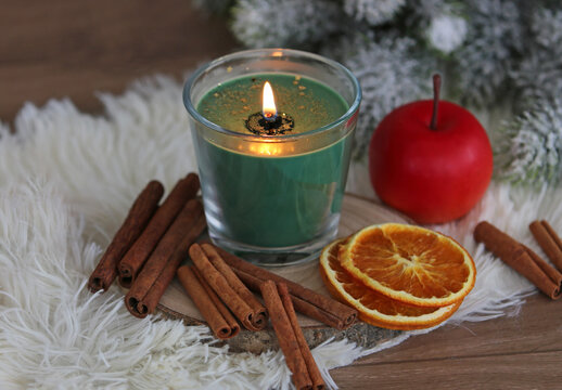 Festive winter decoration featuring a scented candle in a glass jar, spices, and snow-covered fir branches on white faux fur.