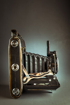 Vintage folding camera with leather bellows on a dark low key background. Antique analog medium format photo equipment, retro photography history concept backdrop.