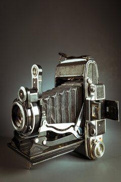 Vintage folding camera with leather bellows on a dark low key background. Antique analog medium format photo equipment, retro photography history concept backdrop.