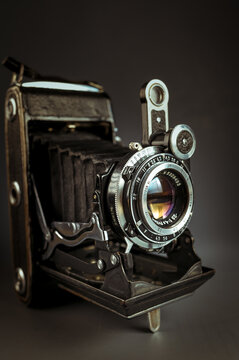 Vintage folding camera with leather bellows on a dark low key background. Antique analog medium format photo equipment, retro photography history concept backdrop.