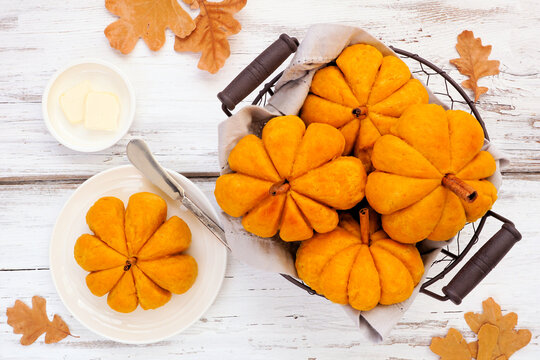 Autumn pumpkin shaped buns. Top down view table scene over a white wood background.