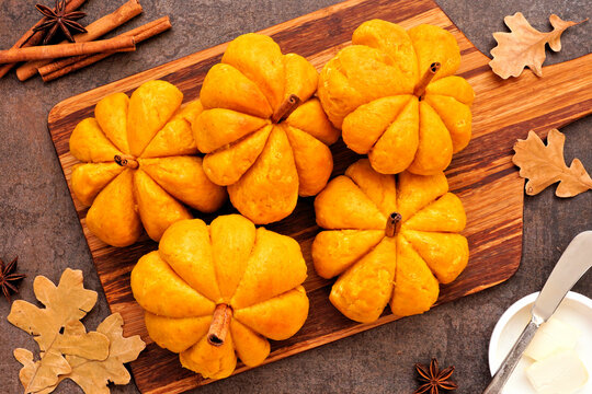 Autumn pumpkin shaped buns. Above view table scene over a dark background.