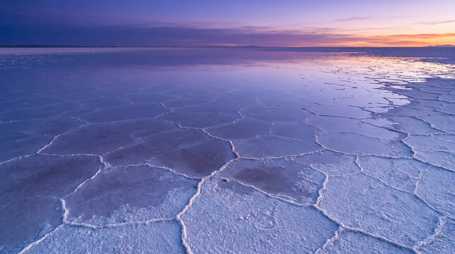 Salt flat landscape with geometric crust patterns under twilight skies.