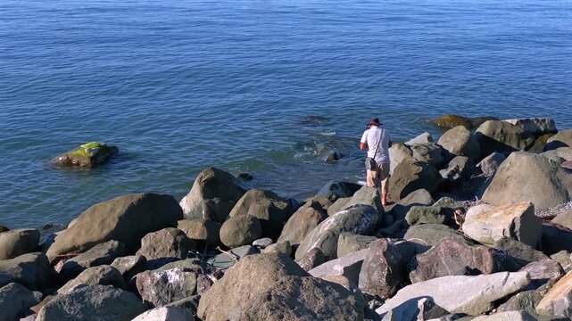 Fisherman fishing in wide coastal view from large rocks beside the Black Sea near Batumi, Georgia, suited for recreational angling, outdoor leisure, coastal tourism and fishing activity content