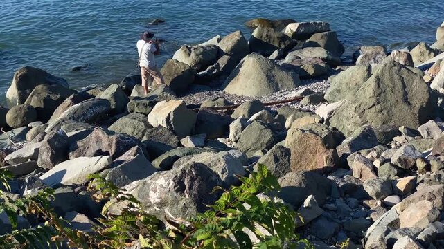 Male fisherman fishing in elevated from large shoreline rocks on the Black Sea near Batumi, Georgia, suited for recreational angling, weekend leisure, local tourism and outdoor hobby content