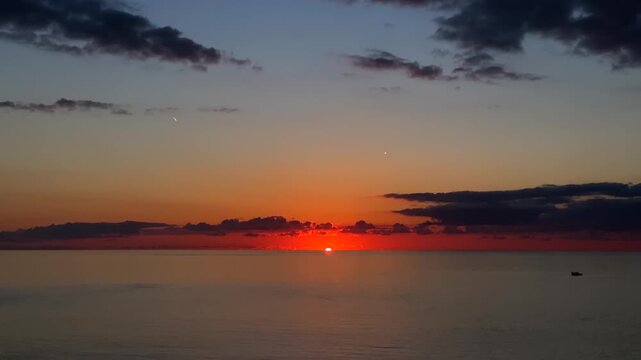 Sun disappearing below horizon, wide view over the sea after sunset with fading orange glow and dark clouds, suited for twilight weather, evening travel, relaxation, meditation and background media