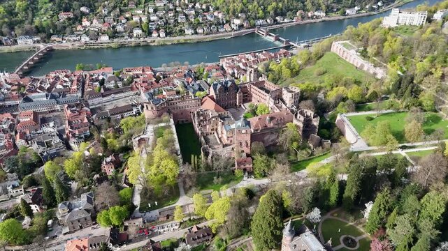 heidelberg castle ruins rise above garden terrace overlooking old town neckar river stone arch old bridge forested hillside wide establishing aerial view drone footage germany baden wurttemberg