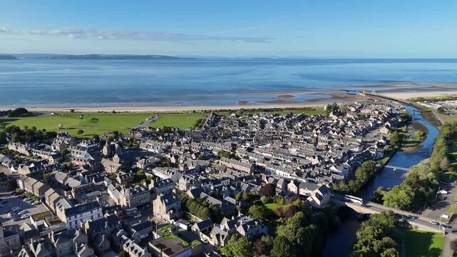High wide aerial drone video of the coastal town of Nairn showing residential architecture, River Nairn, sandy beach, and Moray Firth in Nairnshire, Scottish Highlands, Scotland