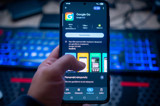 Person hand holding smartphone displaying Google Go app on Play Store screen with blue backlight keyboard background for search engine and internet browsing concept