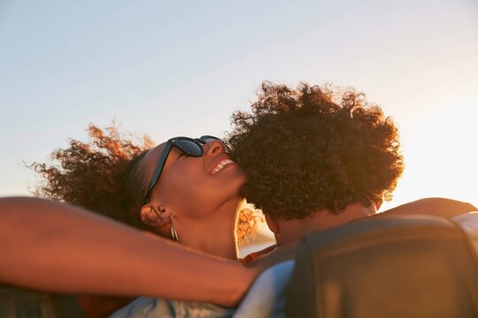 Young couple with curly hair embracing outdoors during a sunny golden hour sunset on a summer day