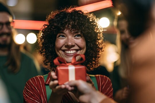 Smiling young woman with curly hair receiving a small red gift box during a festive evening