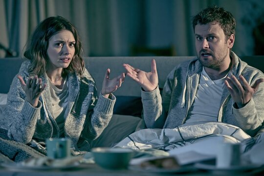 Stressed couple having a heated argument while sitting on a couch in their living room at night