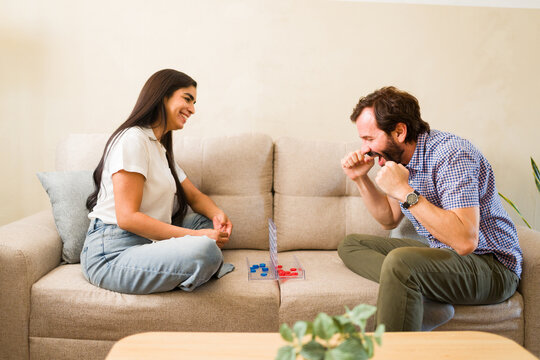 Hispanic couple enjoying a board game at home, man cheering after winning a fun and competitive match
