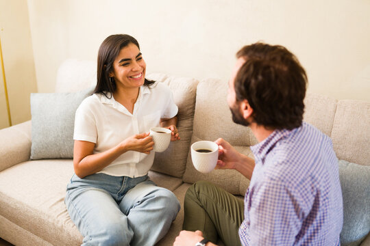 Cheerful couple enjoying coffee and conversation on sofa, dating at home, sharing sweet moments and connection
