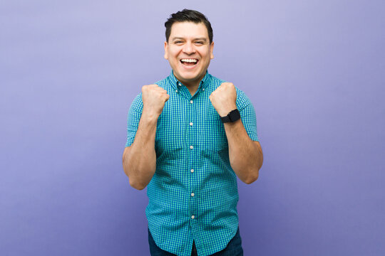Man celebrating victory and achievement with raised fists, expressing happiness and success on purple background