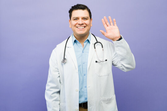 Smiling doctor waving hand, welcoming patients and offering medical assistance in healthcare setting