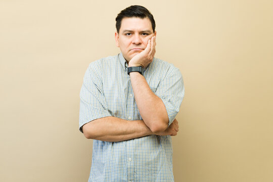Mature man feeling bored and fed up, resting hand on cheek, expressing sadness, disappointment, and disinterest
