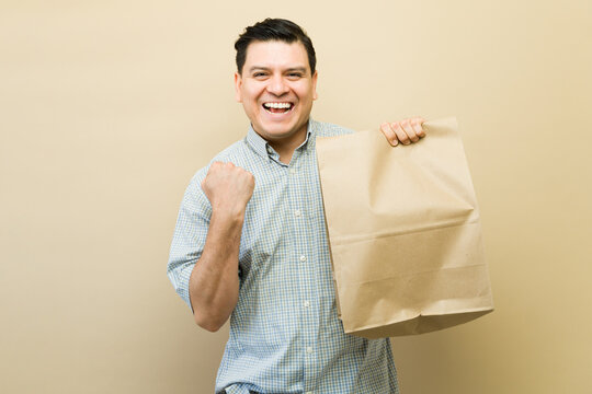 Happy man holding paper bag cheering, celebrating successful shopping or receiving a special delivery or gift