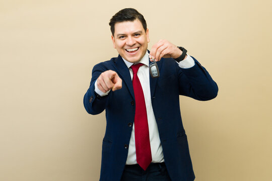 Happy car salesman holding new car keys and pointing finger, offering great deal and welcoming customer