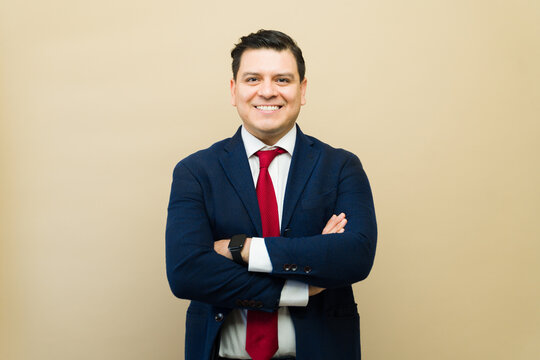 Hispanic businessman smiling at camera, wearing a suit and red tie, showing confidence and leadership