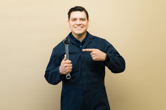 Male mechanic in uniform smiling, holding a wrench, pointing at his chest, symbolizing reliable automotive repair service