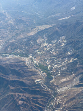 Aerial shot of a dry mountain valley with winding roads, scattered structures, and sun-bleached washes cutting through hillsides, Agua Dulce area, California
