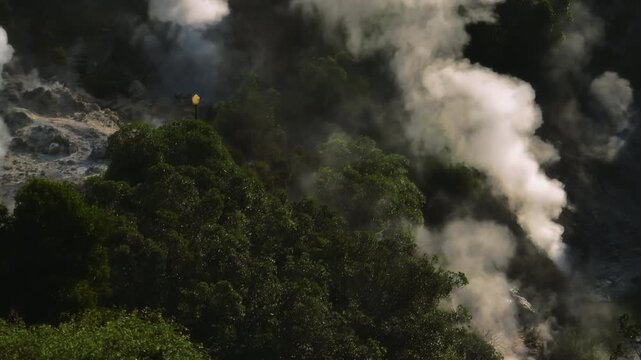 Close-up aerial view of thick volcanic steam plumes rising from geothermal vents within a dense forest area in Furnas, Sao Miguel Island.